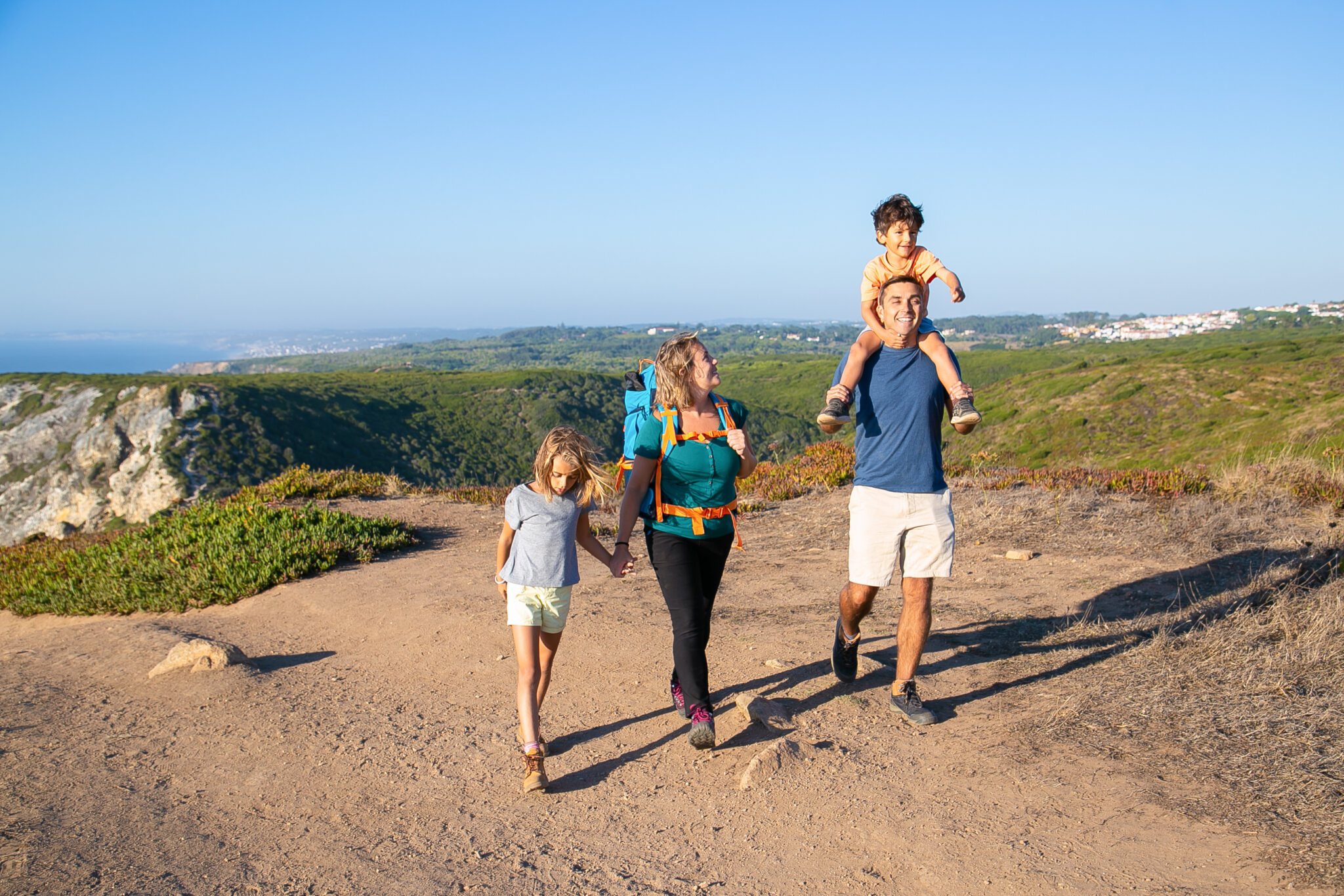 Familia caminando por un sendero de campo con el niño a hombros de su padre